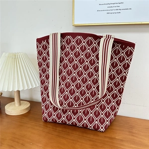 Detail of red knitted tote bag with geometric diamond pattern and striped shoulder strap