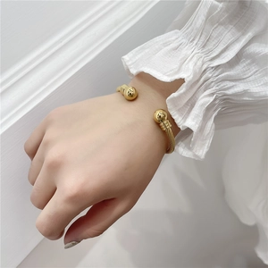 Close-up of gold twisted cable open bangle with polished ball ends on a female wrist
