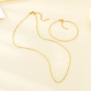 Dettaglio del set collana e bracciale in acciaio placcato oro 18K su tessuto beige