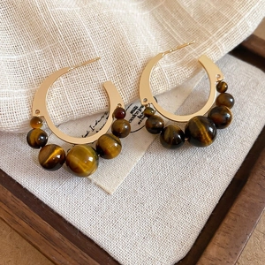 Close-up of vintage 18k gold earrings with tiger eye beads on rustic linen fabric