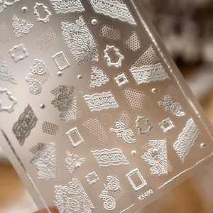 Macro shot of 3D embossed white lace nail stickers with pearl details and vintage patterns