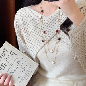 Close-up of layered gold necklace with enamel pendants on a knitted sweater