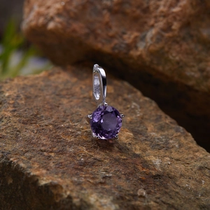 Macro view of S925 silver pendant with round faceted purple gemstone on a rock