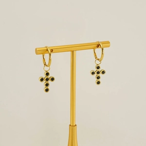 Close-up of golden cross hoop earrings with black zircon stones on a display stand