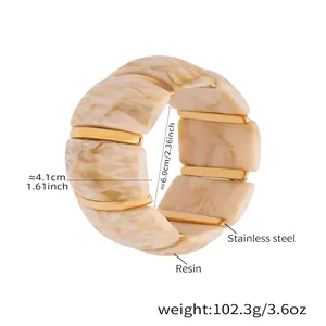 Dettaglio macro di un ampio bracciale in resina effetto marmo con barre d'oro acciaio