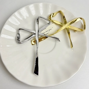 Elegant metallic bow brooches in gold and silver finish on a white ripple plate