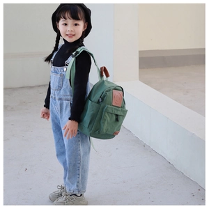 Side view of a green canvas toddler backpack featuring a leather smile patch in a minimalist setting