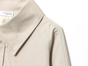 Dettaglio del risvolto del trench beige che mostra l'etichetta S e la trama del twill