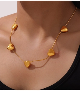 Close-up of a gold-tone snake chain necklace featuring five dainty heart pendants on a model