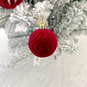 Gros plan d'une boule de Noël en velours rouge avec texture ondulée sur une branche