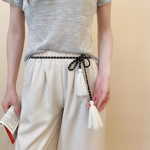Detail of black and white woven waist rope with elegant long white tassels on a grey shirt