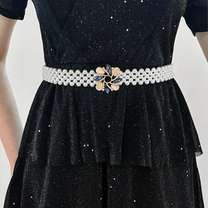 Detail of white pearl woven belt with floral crystal buckle on a black sequin dress