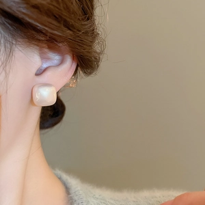 Close-up of model wearing gold plated square sugar pearl stud earrings with a glossy finish