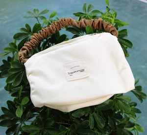 Detail of white corduroy tote bag with brown pleated handle on green leaves