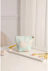 Detail of light blue floral jacquard makeup bag with gold zipper and flower charm