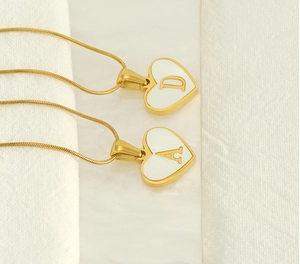 Detail of 18K gold heart necklaces featuring white shell inlay and letters D and A