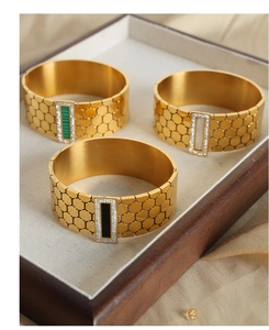 Macro detail of hexagonal hollow gold plated bangles with green, white, and black inserts