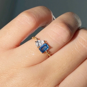 Macro detail of gold-plated open ring with pear-cut white and rectangular blue zircons