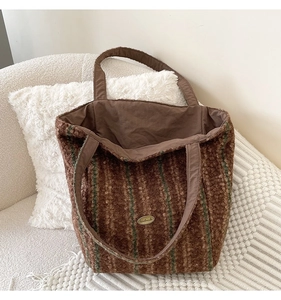 Detail of green and brown striped plush tote bag with handmade metal plaque on soft sofa
