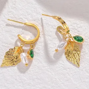 Gold stainless steel earrings set with leaf charms, green gems and drop pearls on white stone