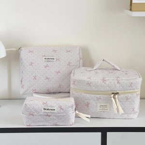 Three-piece quilted cosmetic bag set with pink polka dots and bow pattern on white desk