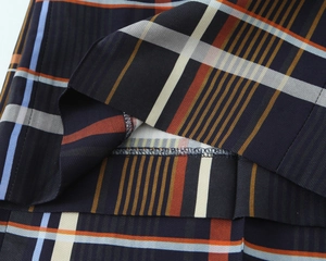 Makroaufnahme von marineblauem Karostoff mit orangen Streifen und hochwertigen Doppelnähten