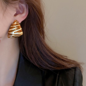 Close-up of triangular gold earrings with amber resin pattern on a model's ear