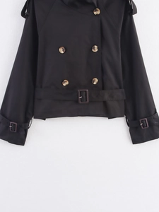 Detail of black double-breasted trench coat featuring resin waist buckle and amber buttons