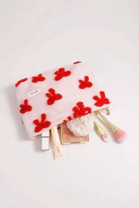 Pink plush cosmetic bag with red bow detail showing spilled makeup brushes and cream