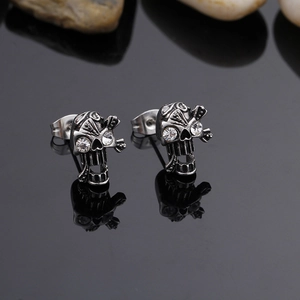 Detailed close-up of skull stud earrings with crystal eyes on a reflective black surface