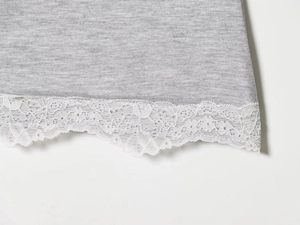 Detailaufnahme von grauem Strickstoff mit weißer floraler Spitzenkante am Saum
