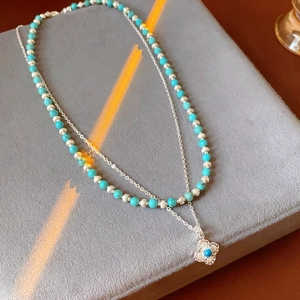 Detail of double-layer necklace with turquoise beads and clover pendant on velvet