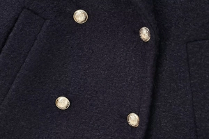 Detail of premium wool blend coat featuring embossed gold metal buttons on textured fabric