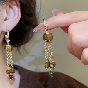 Detail of vintage gold earrings with tiger eye beads and metallic tassels on a model