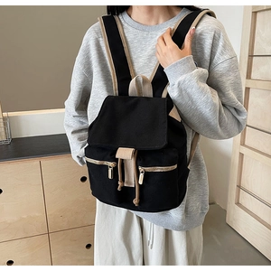 Detalle de la mochila de lona negra con correas blanco crema y dos bolsillos delanteros de cremallera