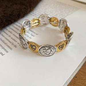 Macro shot of vintage stretch heart bracelet with LOVE engraving on silver and gold rings