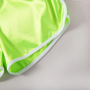 Detail view of neon green satin sports shorts featuring white contrast binding and smooth texture