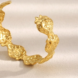 Macro side view of golden strawberry shaped cuff bracelet with textured metallic surface