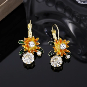 Détail de boucles d'oreilles fleur dorée avec feuilles vertes et grands cristaux