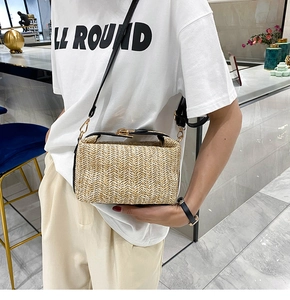 Close-up of beige woven straw crossbody bag featuring black strap and golden metal lock