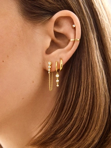 Detailed close-up of 18K gold earrings set with chain and zircon on a model's ear