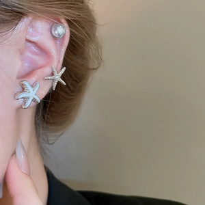 Close-up of starfish-shaped silver earrings and pearl studs worn on ear with soft warm tones