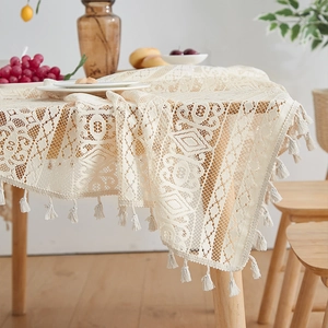 Detail of beige crochet tablecloth featuring geometric patterns and fringed edges on wood