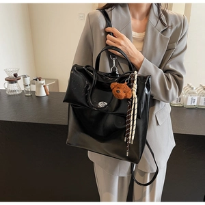 Detail of a black glossy leather backpack with a cute brown plush bear charm