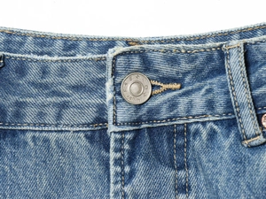 Nahaufnahme des Metallknopfes mit Fashion Denim Gravur auf blauer Distressed-Jeans