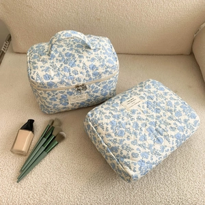 Blue floral cosmetic bags with quilted texture shown with makeup brushes and foundation