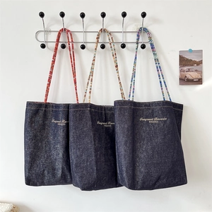 Detailed view of dark blue denim tote bags with colorful braided rope straps and gold logo