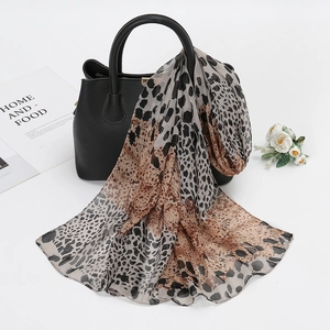 Leopard print chiffon scarf elegantly draped on a black leather handbag detail