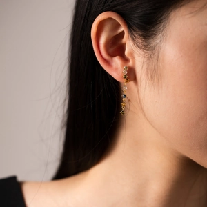 Close-up of elegant gold tassel earrings with colorful gemstones worn by a model