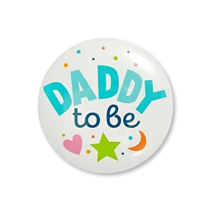 Macro shot of 'DADDY to be' tinplate badge with colorful dots and stars for baby shower